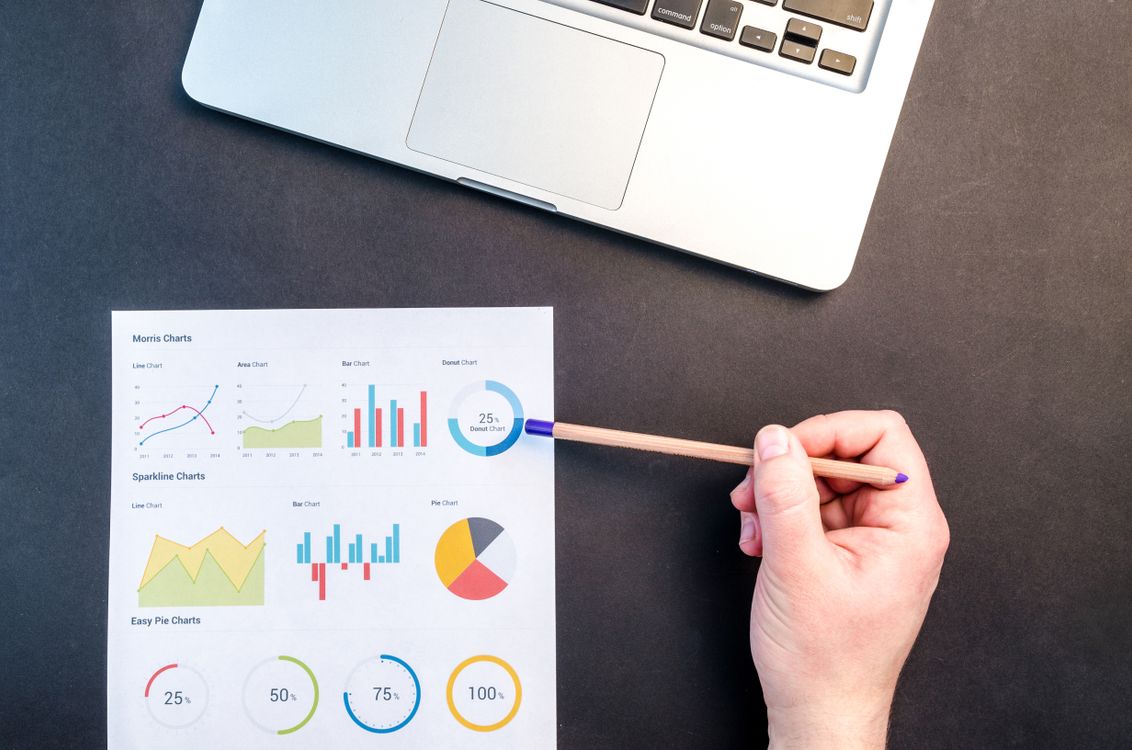 Hand holding a pencil while reviewing colorful data charts on a desk with a laptop